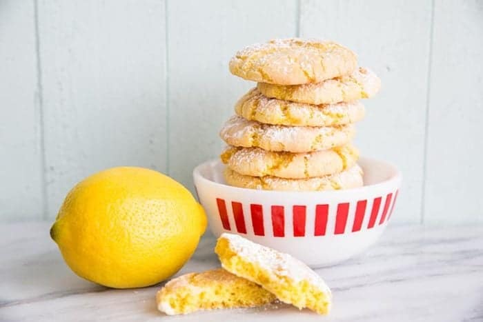 stack of Lemon Crinkle Cake Cookies in a white bowl with red prints, fresh lemon beside it
