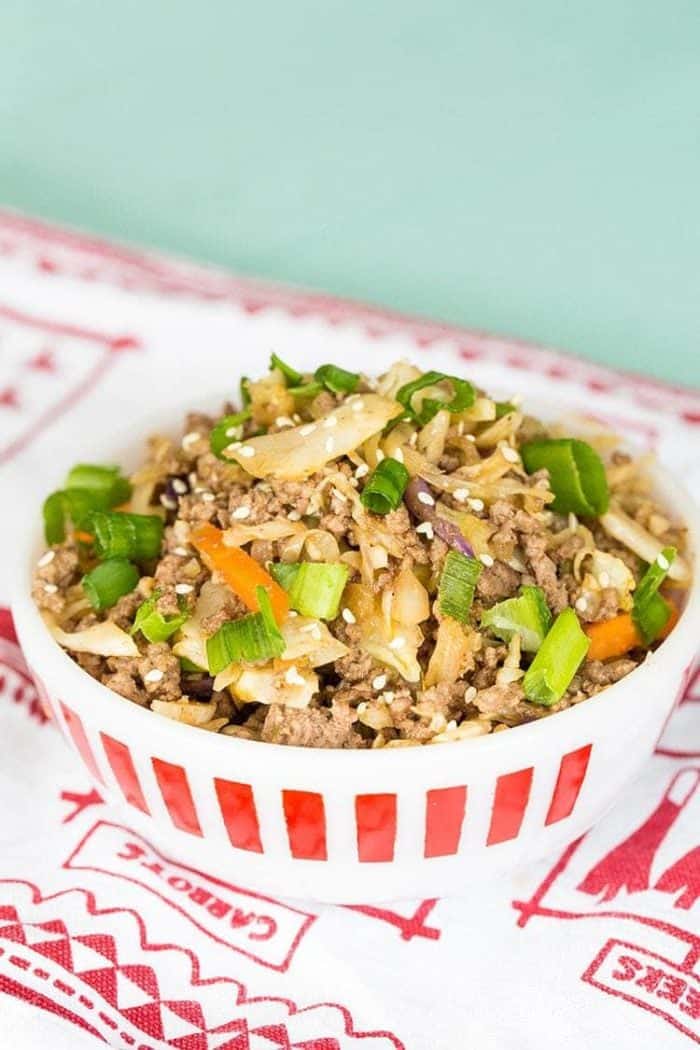 Crack Slaw in a white bowl using ground beef and coleslaw mix, topped with green onions and sesame seeds