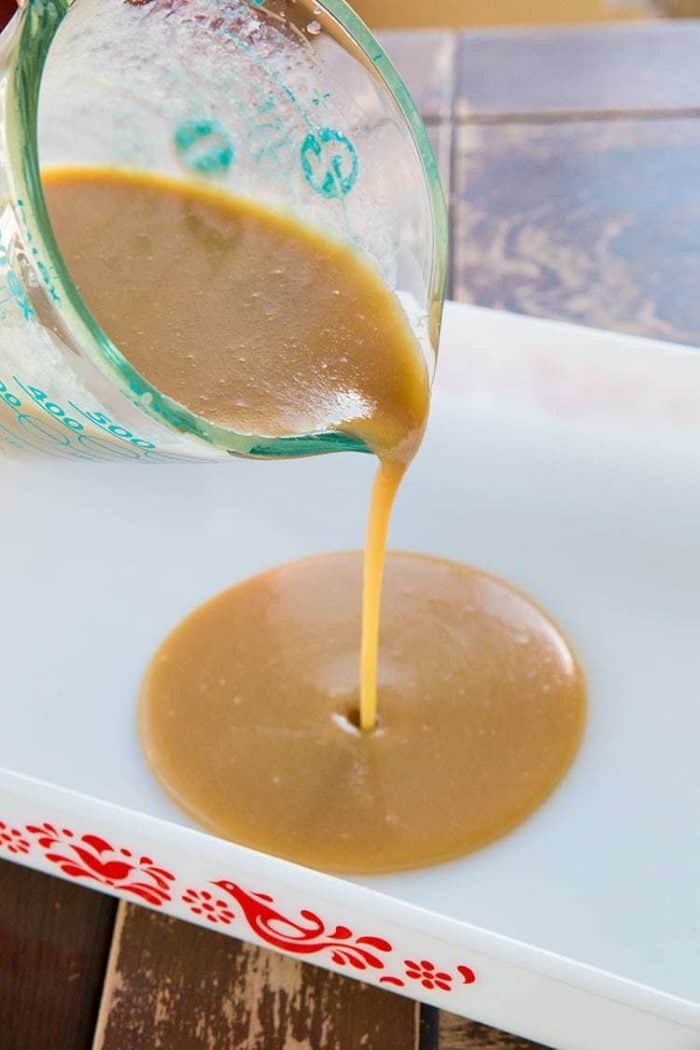 pouring the caramel cream from Pyrex measuring cup into white baking pan