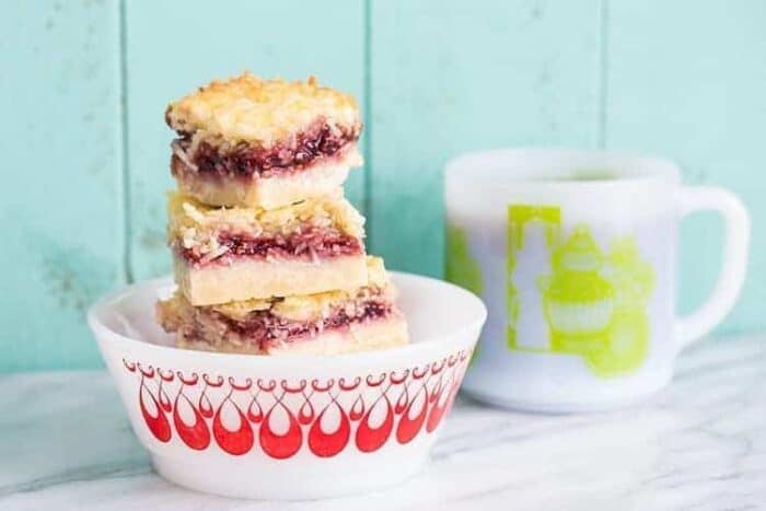 stack of Raspberry Coconut Bars in a white bowl with red prints, white mug with yellow print on background