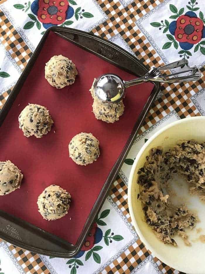 Ice cream scoop size of Walnut Loaded Chunky Chocolate Chip Cookie dough in the parchment lined sheet