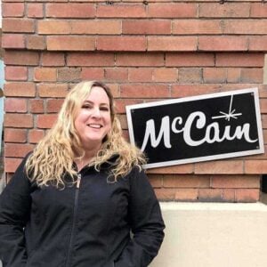 woman wearing black jacket standing near the McCain signage with brick wall on background