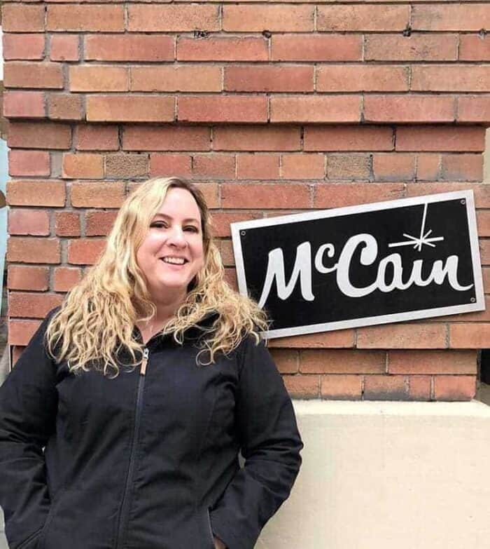 woman wearing black jacket standing near the McCain signage with brick wall on background 
