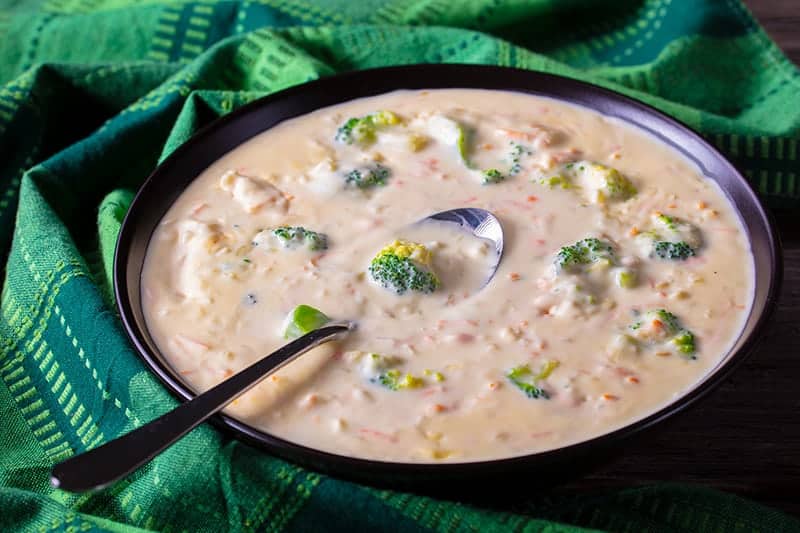 green tablecloth underneath a bowl of Broccoli Cheese Soup with spoon