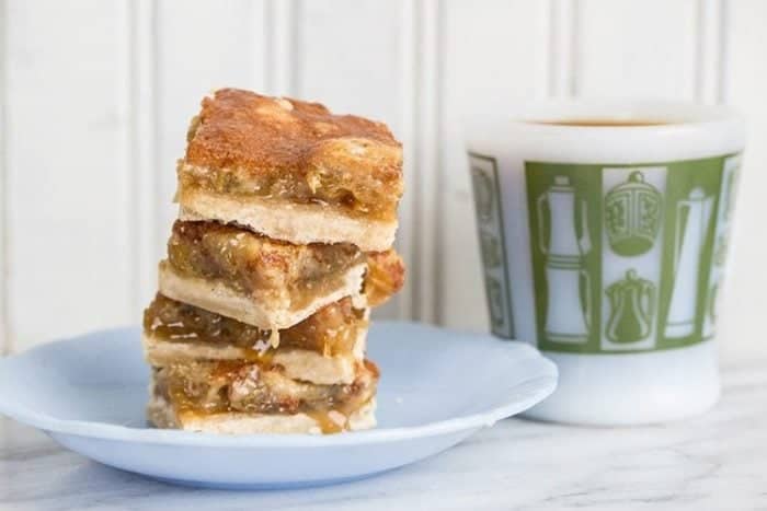 stack of Butter Tart Bars in a dessert plate with a mug on the side in white background