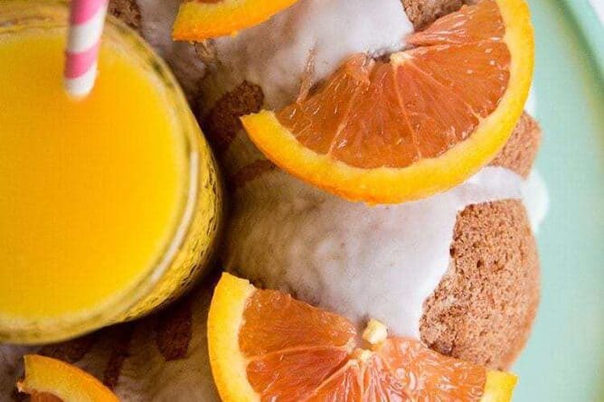 Top down shot of Harvey Wallbanger Cake with Boozy Glaze and slices of oranges on top, a glass of orange juice at the center of bundt cake