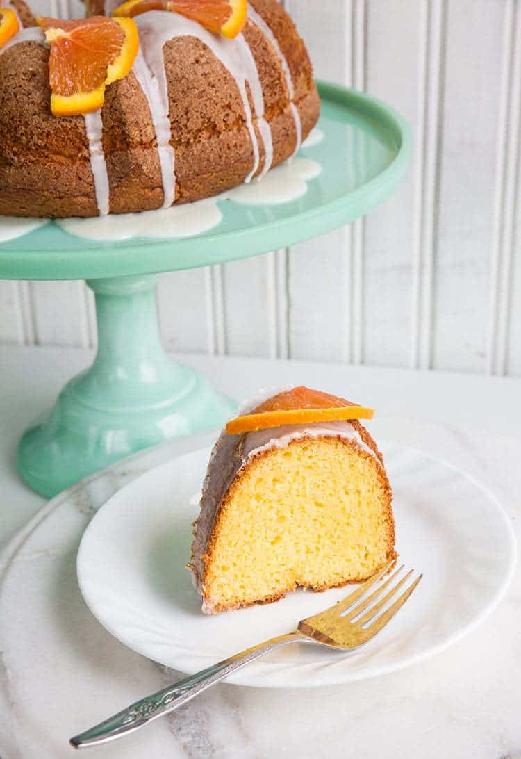 Sliced Harvey Wallbanger Cake with Boozy Glaze and Orange Slices in green cake colder and in a white plate