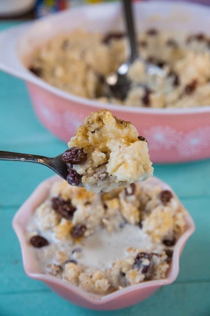 Baked Rice Pudding on a spoon, pink casserole dish with pudding on the background