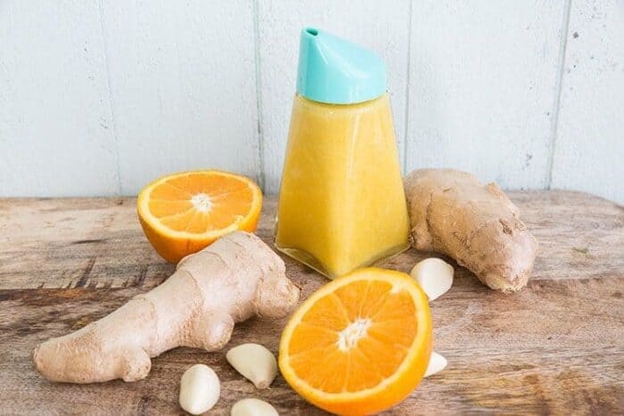 Ginger Sesame Citrus Salad Dressing in a jar with a lid. Sliced orange, ginger and garlic clove around 