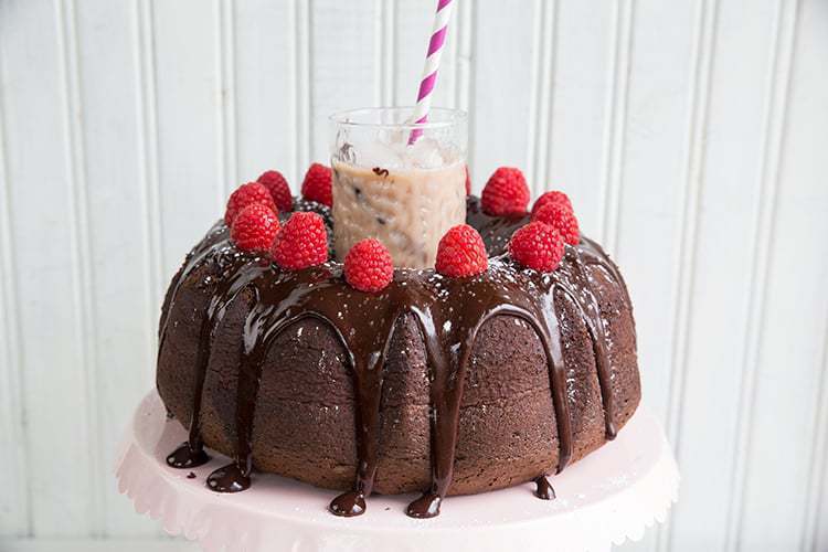 A glass of Raspberry Kahlua Mudslide Cocktail at the middle of Raspberry Kahlua Mudslide Bundt CAKE on white background