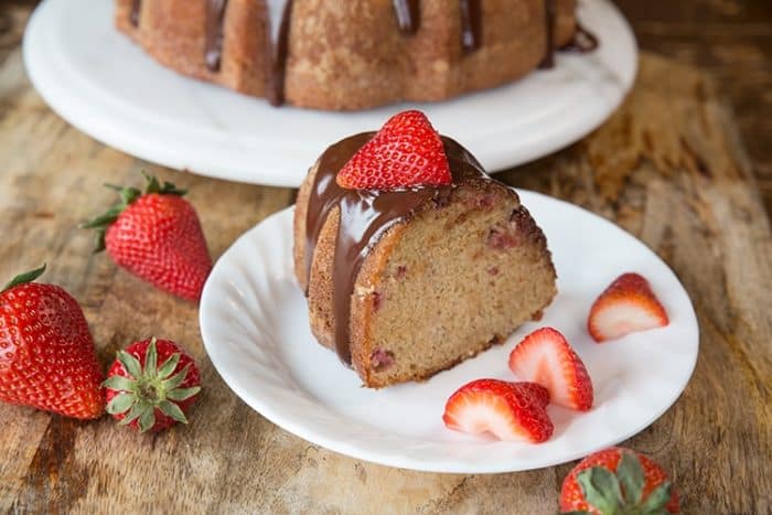 White Dessert plate with a Slice of Strawberry Yogurt Bundt Cake topped with chocolate satin glaze and fresh strawberries