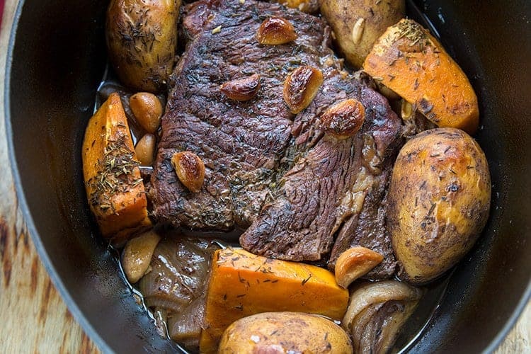 beef roast on a Dutch oven with vegetables around and garlic on top