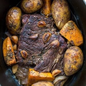 beef roast on a Dutch oven with vegetables around, garlic and thyme on top