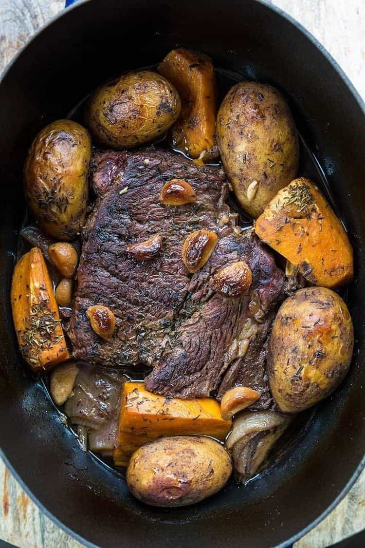 beef roast on a Dutch oven with vegetables around, garlic and thyme on top 