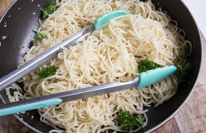 getting some pasta using kitchen tongs in Spaghetti Aglio E Olio in a large skillet with garnished with parsley 