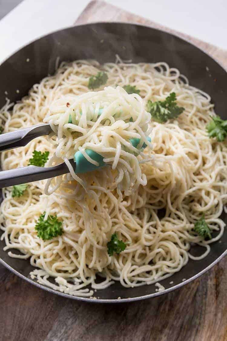 cooked homemade pasta with parsley leaves in a black skillet with tongs 