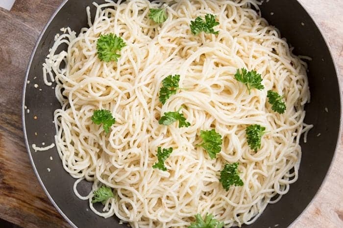 Spagečiai „Aglio E Olio“ didelėje keptuvėje, ant kurios viršaus puošta petražolėmis