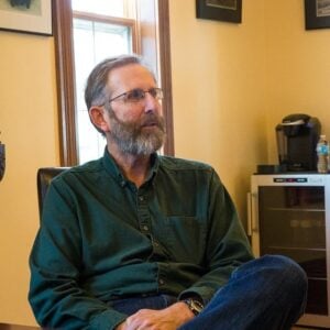 man wearing eye glasses, long sleeves dark green polo shirt, sitting near the table