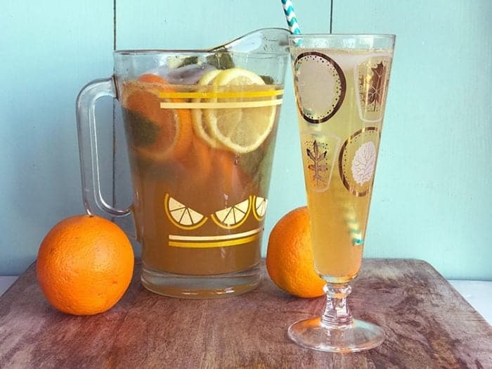 A pitcher and a glass of Sparkling Bourbon Lemonade with slices of oranges