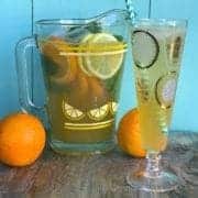A pitcher and a glass of Sparkling Bourbon Lemonade with slices of oranges