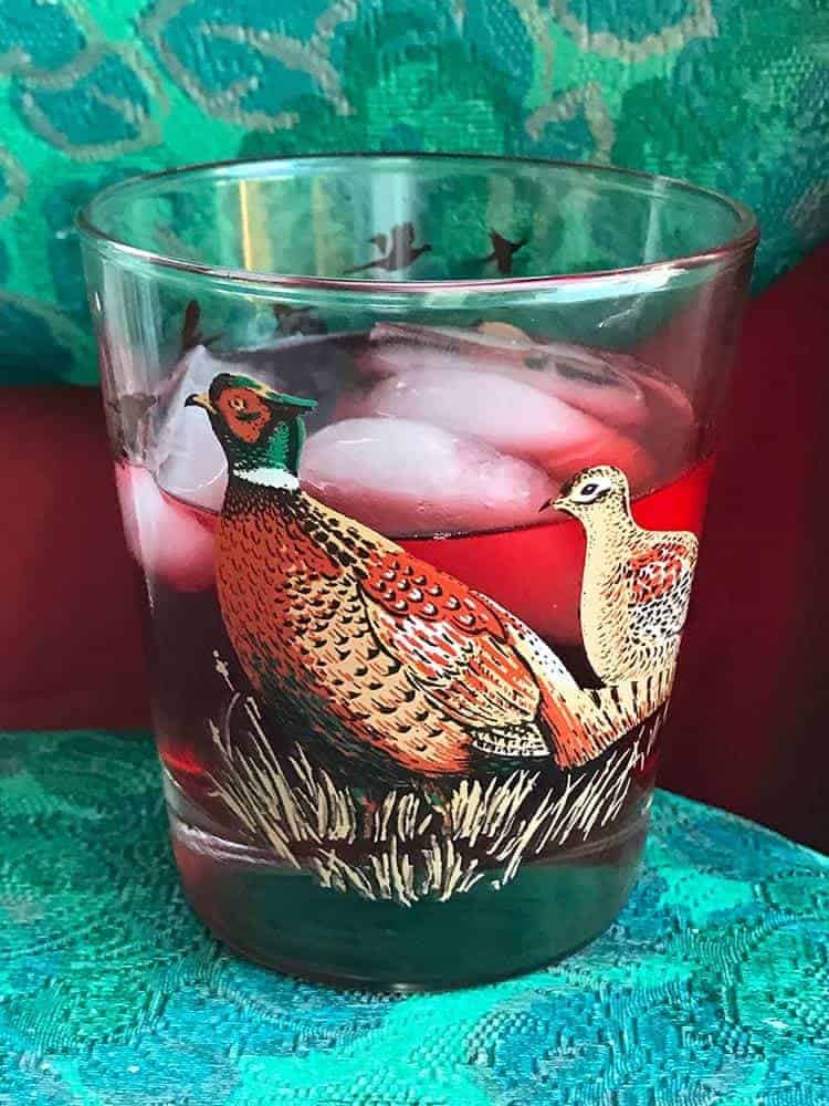 vintage bird glass with oppenheim cocktail and ice on red and green background