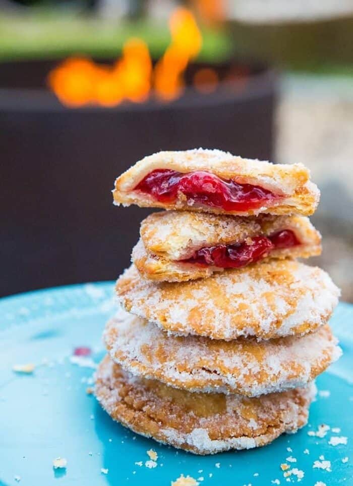 close up of Campfire Cherry Hand Pies in a blue plate with one piece broken into two showing the inside