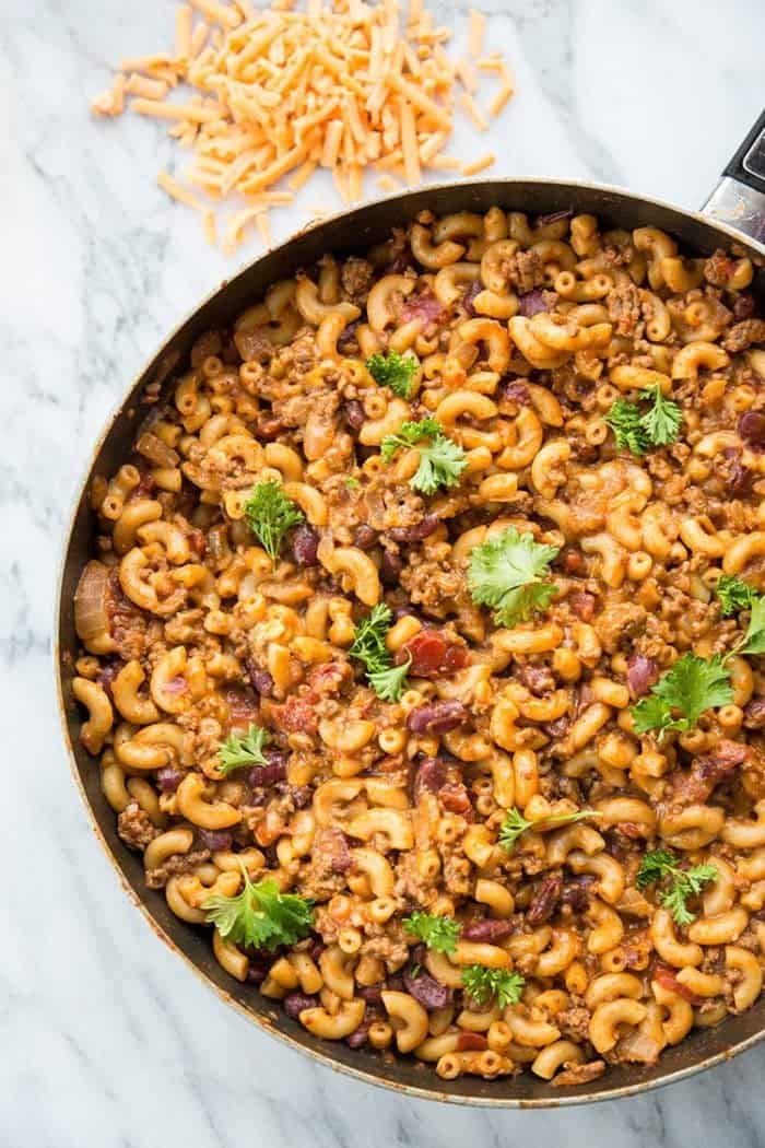 Homemade cheesy chili mac in a large black skillet on a white marble slab