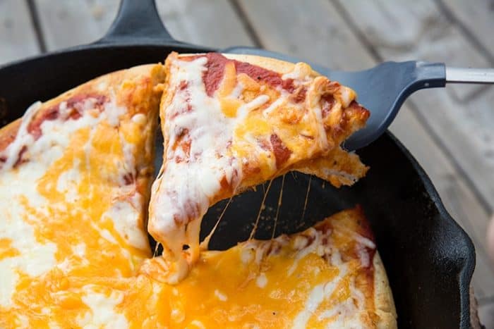 getting a slice of cheesy Campfire Pizza from a flat pan