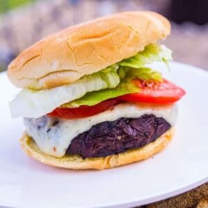 close up of Homemade Portobello Mushroom Burger in white plate with slices of tomatoes and lettuce
