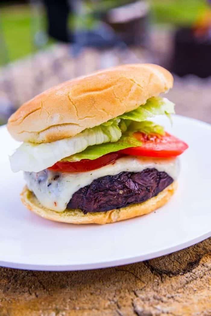 close up of Homemade Portobello Mushroom Burger in white plate with slices of tomatoes and lettuce