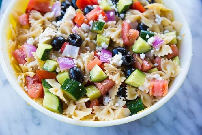 Greek Pasta Salad in a white bowl loaded with vegetables on a marble background