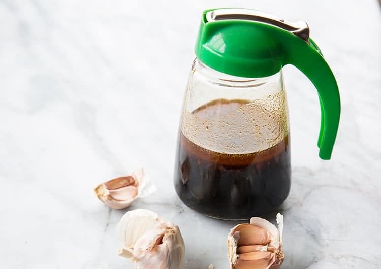 Teriyaki Marinade in a pitcher like container with green color lid, some garlic around on a marble background