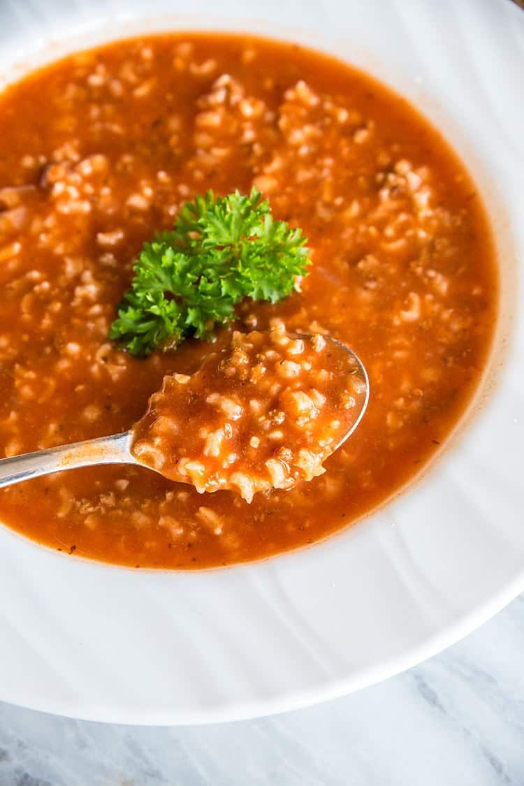 close up of a white plate with Tomato & Rice Hamburger Soup and a spoon in it