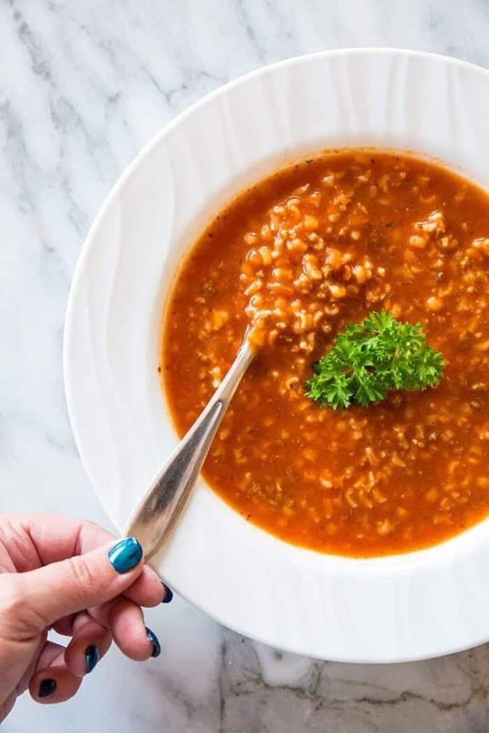 spooning some Tomato & Rice Hamburger Soup in a white plate