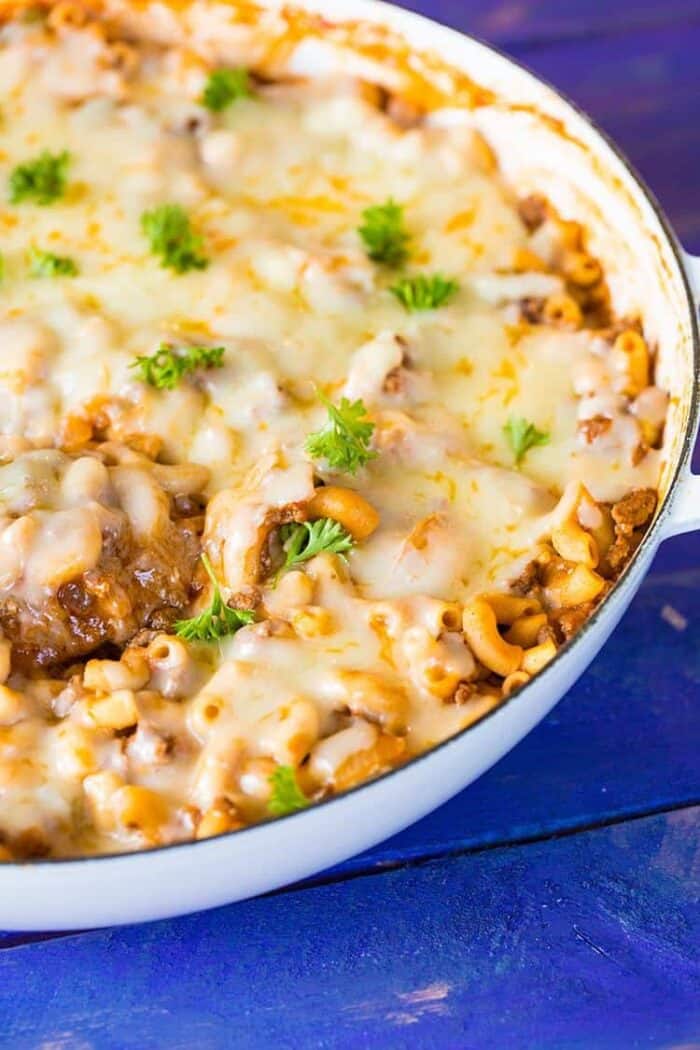 close up of Mac & Cheese in skillet garnish with parsley on blue wood background