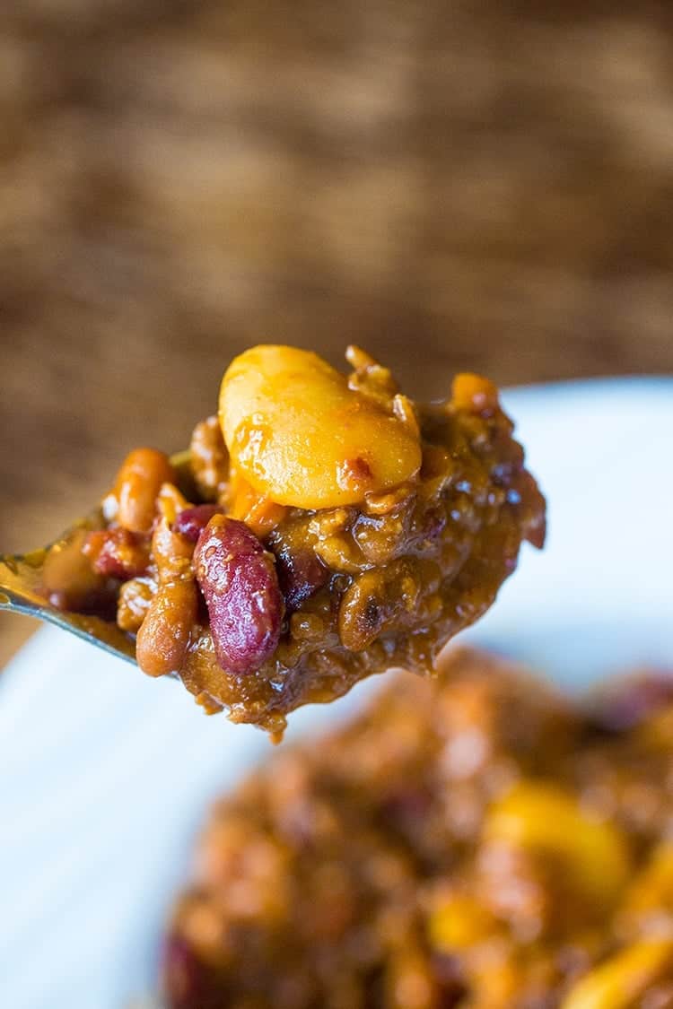 close up of spoon with Slow Cooker Calico Beans from a white bowl