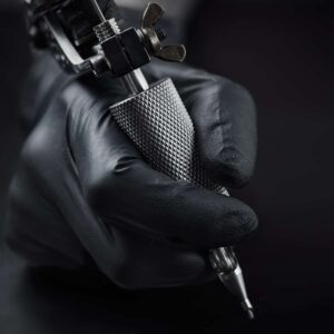 holding a tattooing equipment hands with black glove on dark background