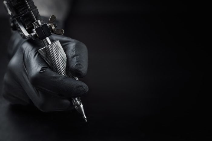 holding a tattooing equipment hands with black glove on dark background