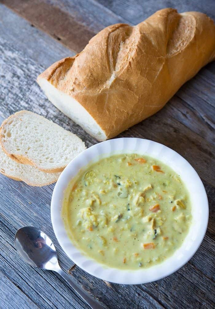 white soup bowl with Crock pot Chicken & Wild Rice Soup and loaf of French bread on side ready to be enjoy!