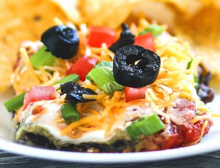 Tex-Mex 7 Layer Dip topped with tomatoes, green onions, shredded cheese and black olives