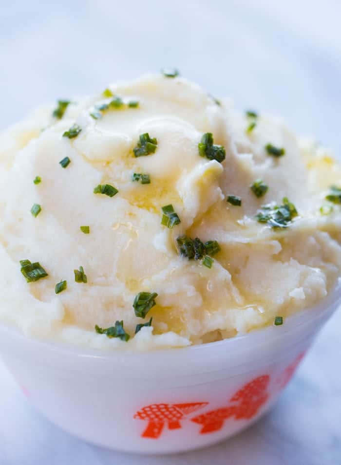 close up of Mashed Potatoes in a white bowl with sprinkle of chopped green onions