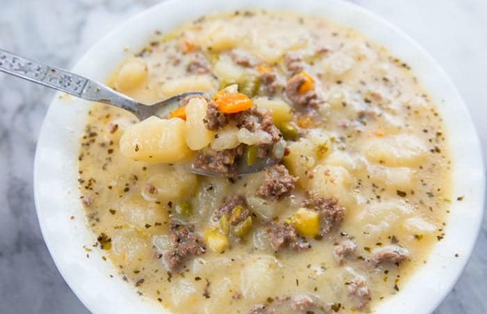creamy potato and hamburger soup in a white soup bowl with a spoon