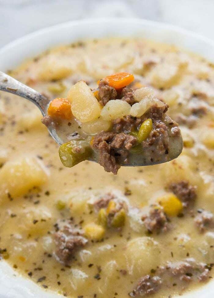 close up of a spoon full of creamy potato and hamburger soup in a white soup bowl