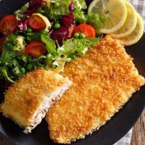 black plate loaded with Air Fryer Fish Fillets garnish with lemon wedges and vegetables