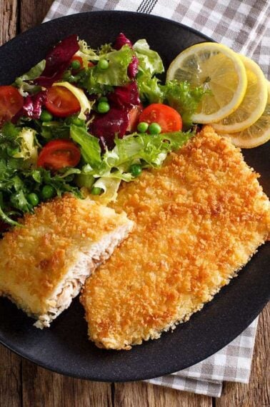 black plate loaded with Air Fryer Fish Fillets garnish with lemon wedges and vegetables