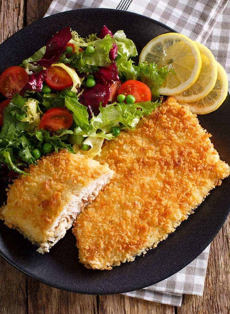 black plate loaded with Air Fryer Fish Fillets garnish with lemon wedges and vegetables