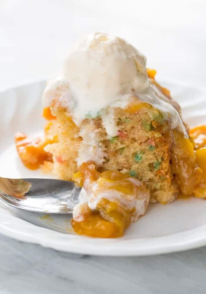 Slice of Confetti Cake in a White Plate Topped with Peach Topping and Vanilla Ice Cream