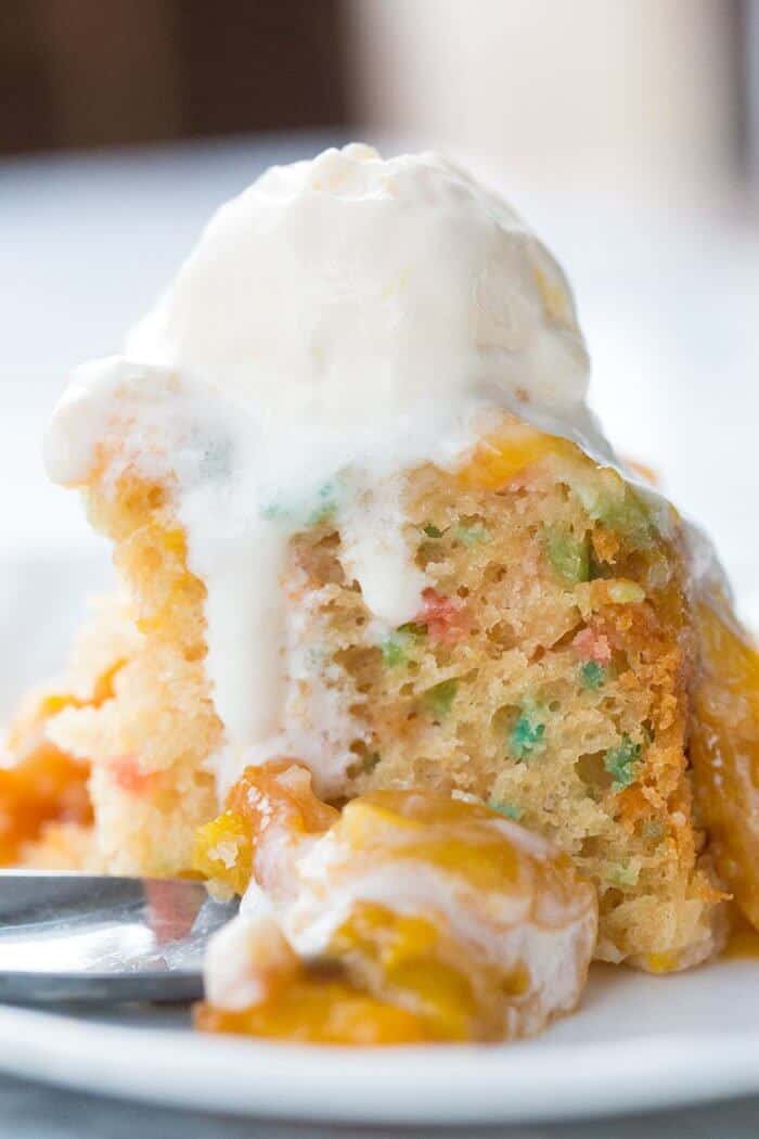 Close up of Confetti Cake in a White Plate Topped with Peach Topping and Vanilla Ice Cream