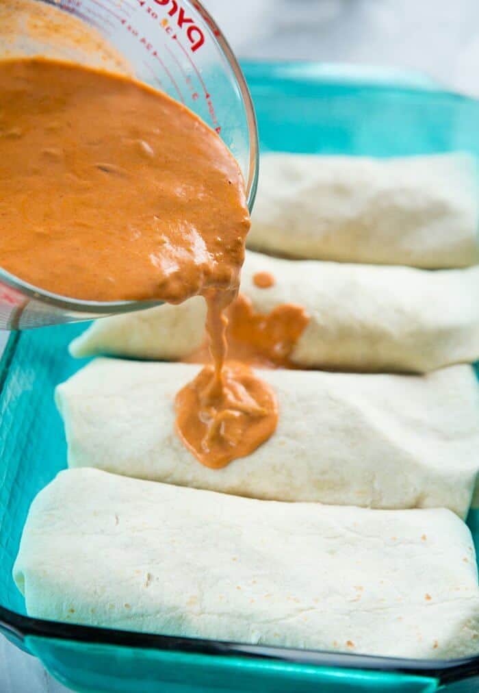 Pouring the sauce over four pieces of wrapped tortillas
