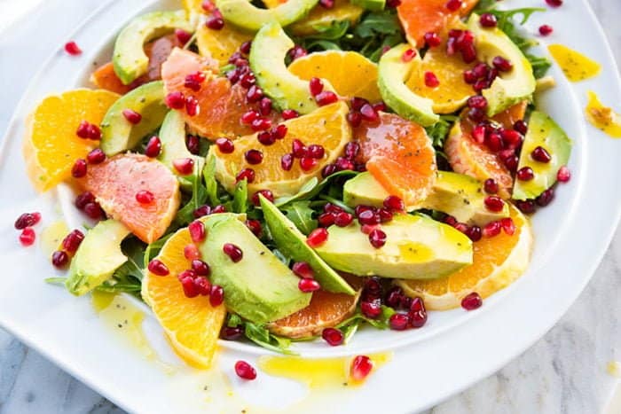Winter Citrus Avocado Salad in a white plate topped with pomegranate arils